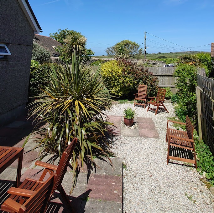 Lebanon Cottage garden with table and chairs, gravel and tiles, palms and shrubs and a clear blue Cornish sky